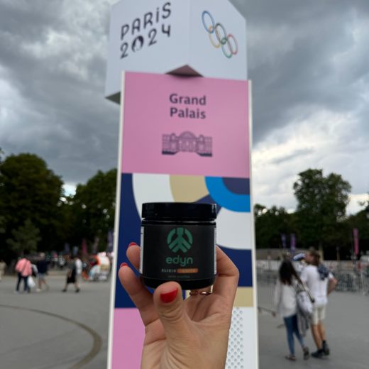 Veronica holding a jar of Edyn Elixir Ignite in front of the Paris 2024 Grand Palais sign